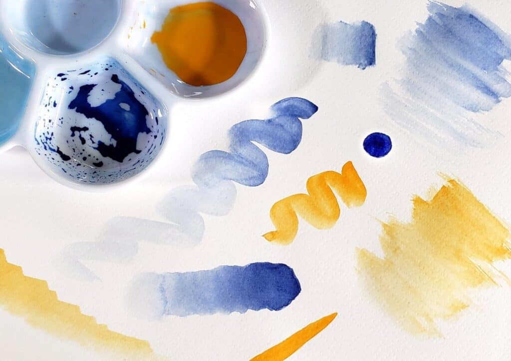 There is a mixing palette next to a piece of watercolor paper that has various brushstrokes on it showing how to practice water control.