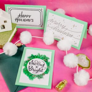 3 Holiday cards laid out on a pink backdrop.